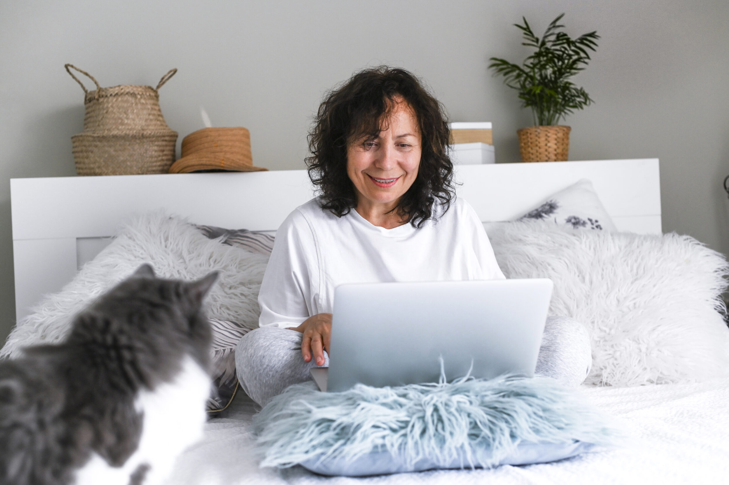 Adult woman with a laptop and cat is sitting on the bed. Modern business lady at home. Photo in light colors. Portrait How It Works in Naperville, IL